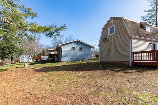 view of property exterior with an outbuilding, a yard, a storage unit, a gambrel roof, and a deck