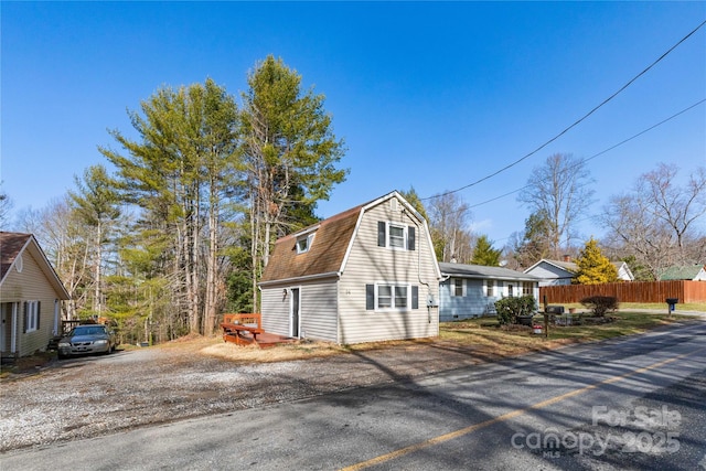 exterior space with a gambrel roof, driveway, and fence