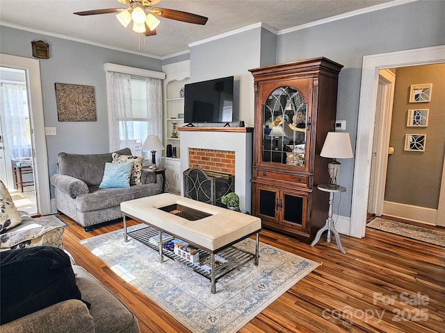 living room featuring a fireplace, wood finished floors, a ceiling fan, baseboards, and ornamental molding