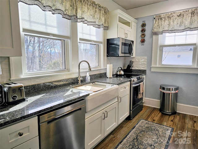 kitchen featuring dark wood-type flooring, a sink, baseboards, appliances with stainless steel finishes, and backsplash