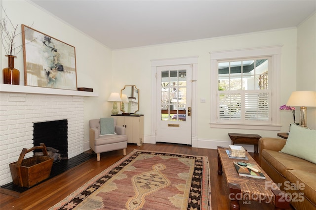 living area with baseboards, crown molding, wood finished floors, and a brick fireplace