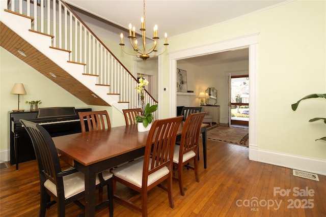 dining space with wood-type flooring, ornamental molding, baseboards, visible vents, and a notable chandelier