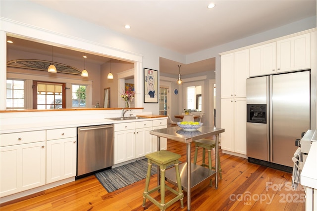 kitchen featuring appliances with stainless steel finishes, white cabinetry, a sink, light wood-style floors, and pendant lighting