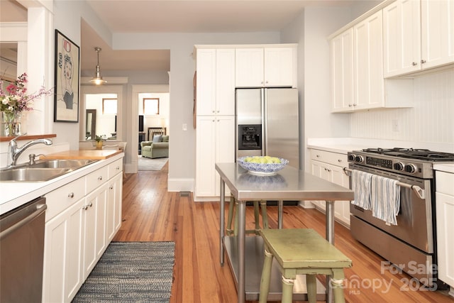 kitchen featuring white cabinetry, light countertops, light wood-type flooring, a sink, and appliances with stainless steel finishes