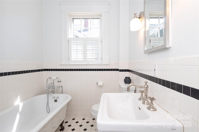 bathroom with tile patterned flooring, toilet, a soaking tub, a wainscoted wall, and a sink