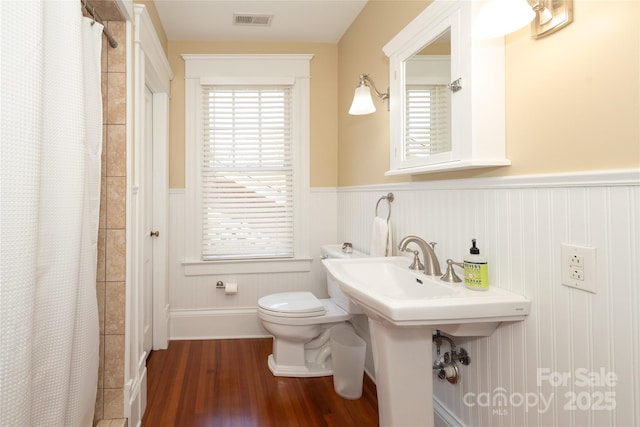 bathroom with a wainscoted wall, visible vents, a shower with shower curtain, toilet, and wood finished floors