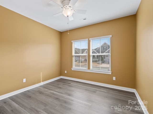 spare room with a ceiling fan, visible vents, baseboards, and wood finished floors