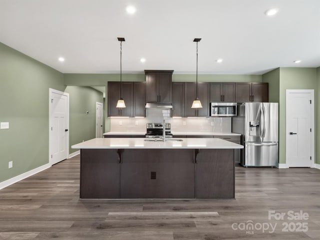 kitchen with a center island with sink, appliances with stainless steel finishes, light countertops, under cabinet range hood, and a sink