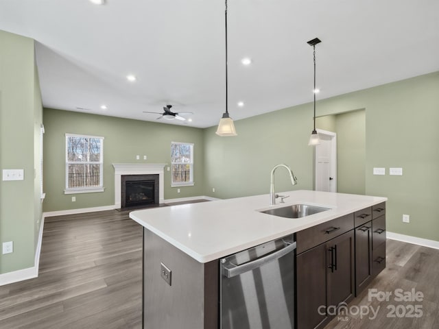 kitchen with dark brown cabinetry, dishwasher, a fireplace with flush hearth, dark wood-style flooring, and a sink