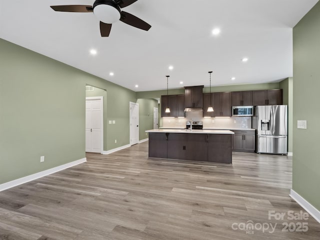 kitchen with light wood finished floors, stainless steel appliances, dark brown cabinets, and light countertops