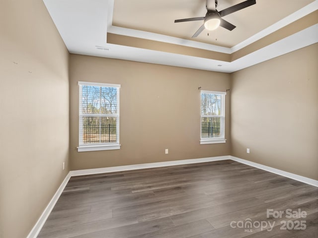 empty room with a raised ceiling, baseboards, and wood finished floors