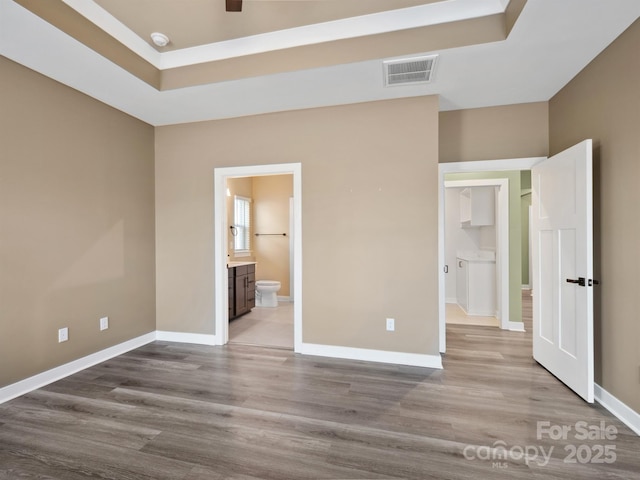 unfurnished bedroom featuring visible vents, ensuite bathroom, baseboards, and wood finished floors