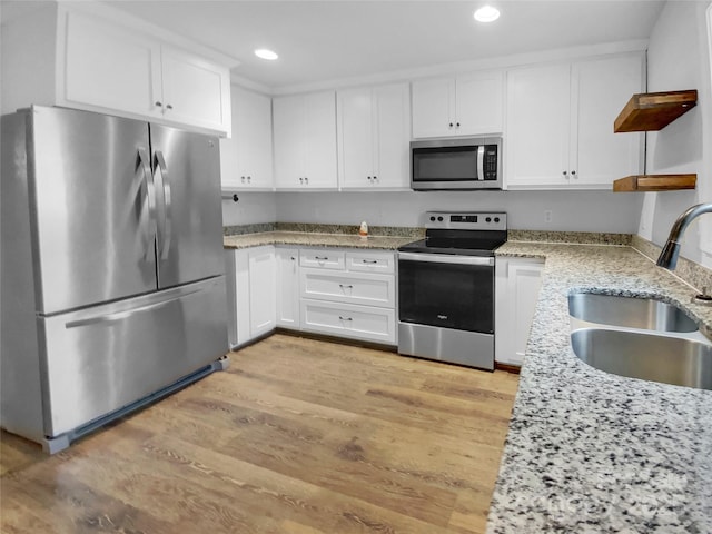 kitchen with light wood-type flooring, appliances with stainless steel finishes, white cabinets, and a sink