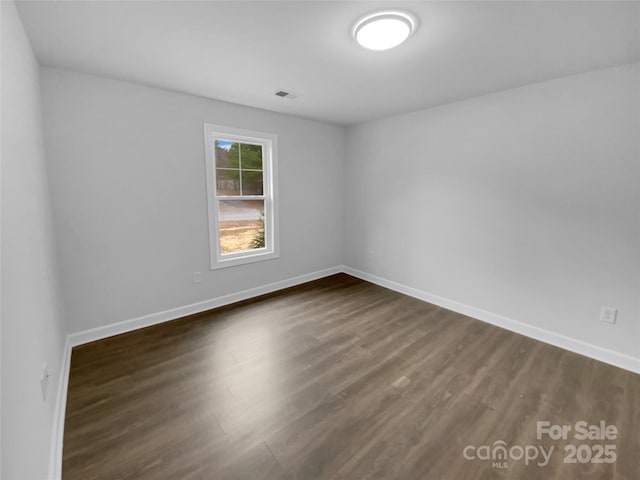 unfurnished room with visible vents, dark wood finished floors, and baseboards