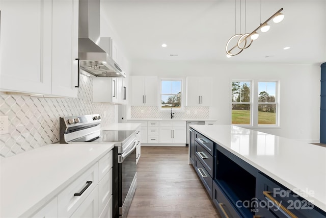 kitchen featuring tasteful backsplash, light countertops, white cabinets, stainless steel range with electric cooktop, and wall chimney exhaust hood