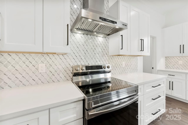 kitchen with light countertops, decorative backsplash, stainless steel range with electric cooktop, white cabinetry, and wall chimney range hood