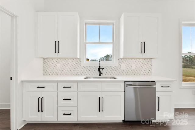 kitchen with light countertops, backsplash, stainless steel dishwasher, white cabinets, and a sink