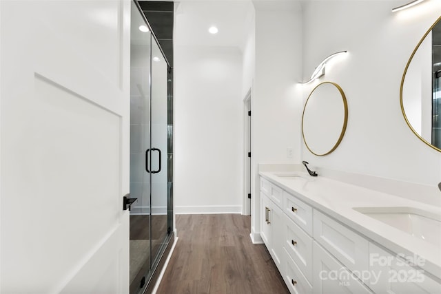 full bath with a stall shower, double vanity, a sink, and wood finished floors