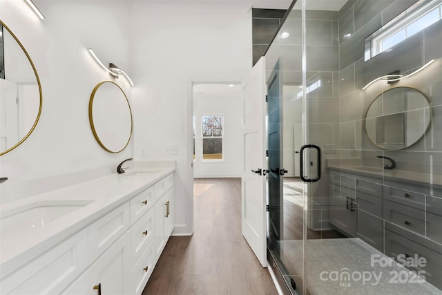 bathroom with double vanity, wood finished floors, a stall shower, and a sink