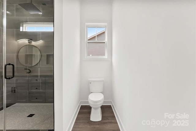 bathroom featuring wood finished floors, a tile shower, toilet, and baseboards