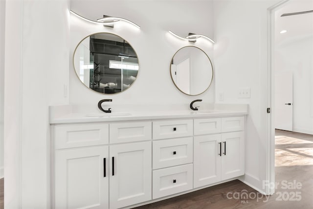 bathroom with double vanity, wood finished floors, a sink, and baseboards