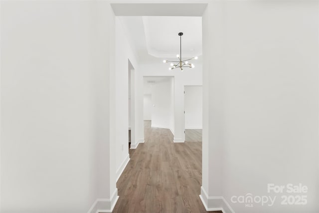 hallway with an inviting chandelier, baseboards, and wood finished floors