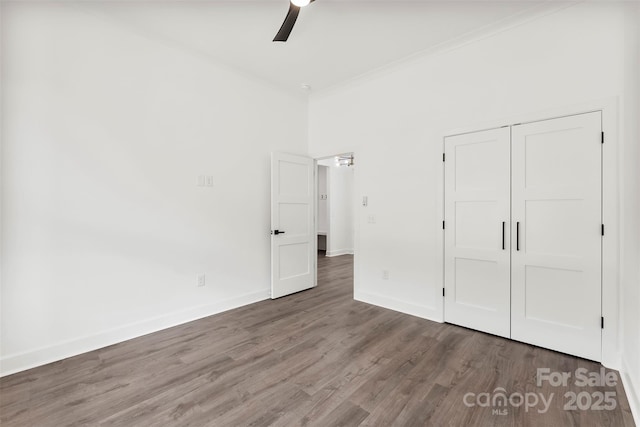 unfurnished bedroom with a closet, baseboards, wood finished floors, and ornamental molding