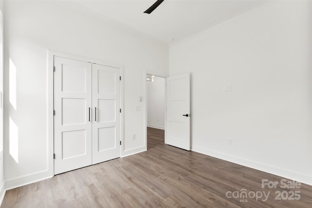 unfurnished bedroom with a closet, wood finished floors, a ceiling fan, and baseboards