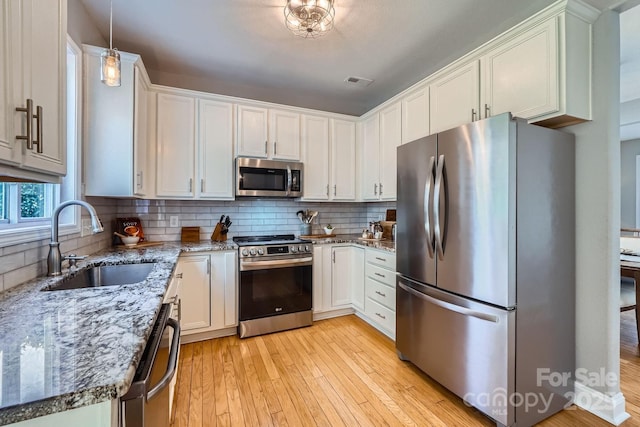 kitchen featuring a sink, visible vents, appliances with stainless steel finishes, light wood-type flooring, and light stone countertops