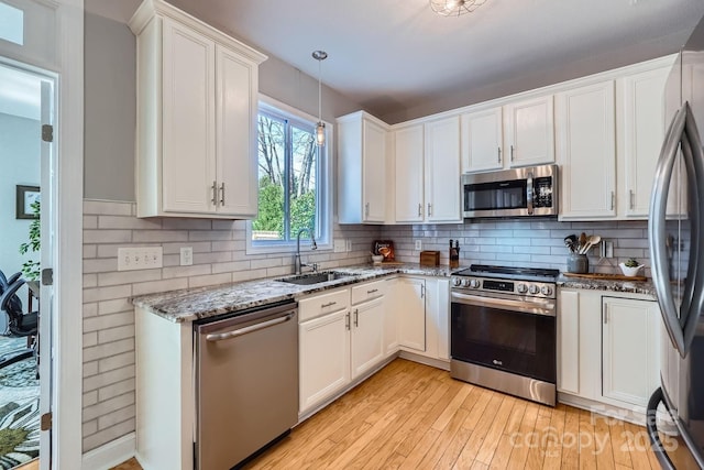 kitchen featuring stainless steel appliances, a sink, white cabinetry, light stone countertops, and tasteful backsplash