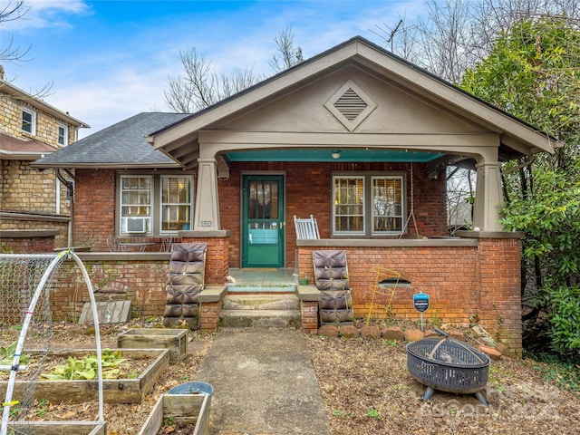 view of front of property featuring an outdoor fire pit, a garden, roof with shingles, and brick siding