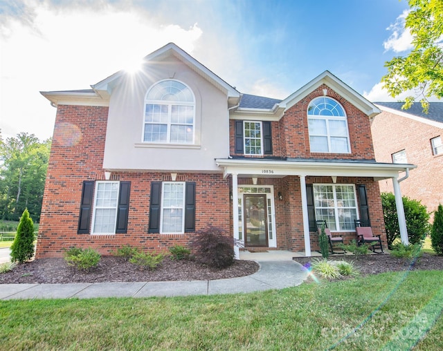 traditional home with a front yard, covered porch, brick siding, and stucco siding