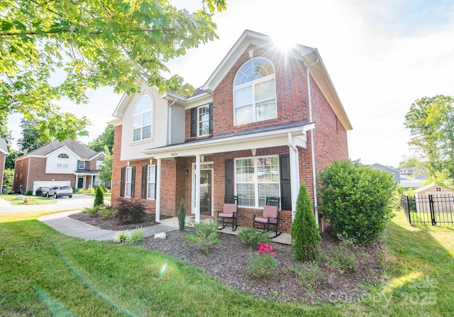 traditional home with covered porch, brick siding, a front yard, and fence