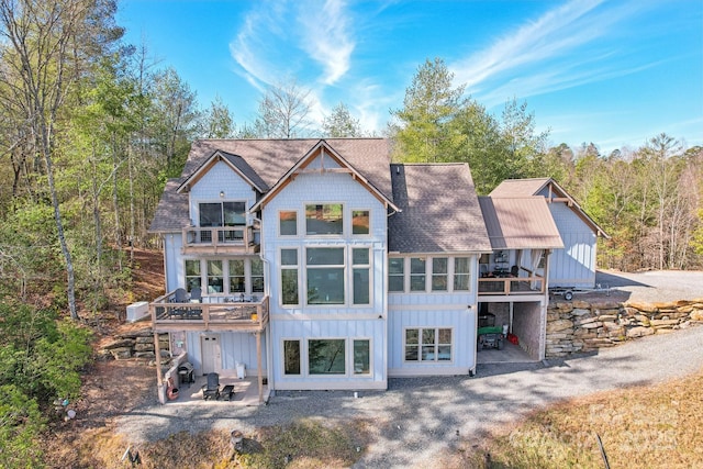 back of property with a balcony, a patio area, and board and batten siding