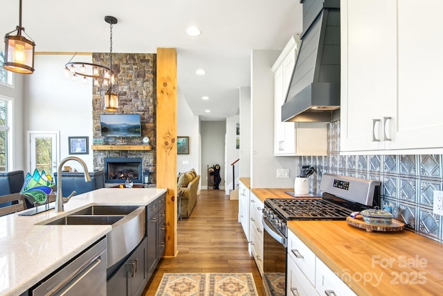 kitchen with a fireplace, butcher block counters, custom range hood, appliances with stainless steel finishes, and open floor plan