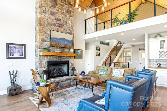 living area with a high ceiling, a fireplace, wood finished floors, baseboards, and stairs