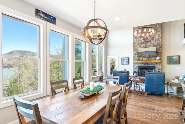 dining space featuring a wealth of natural light, wood finished floors, a notable chandelier, and a stone fireplace