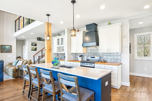 kitchen featuring custom range hood, a sink, stainless steel gas range, white cabinetry, and backsplash