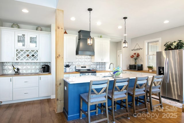 kitchen with white cabinets, appliances with stainless steel finishes, custom exhaust hood, light countertops, and a kitchen bar