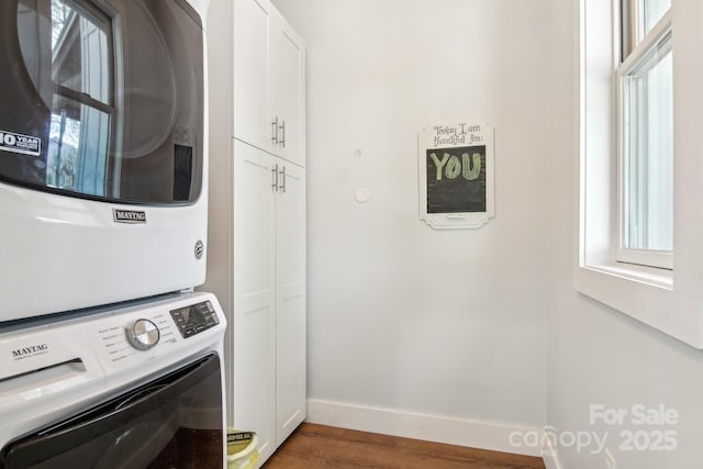 laundry room with cabinet space, baseboards, stacked washer / drying machine, and wood finished floors