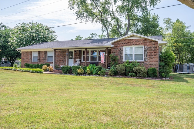 ranch-style house featuring a trampoline, covered porch, brick siding, and a front lawn