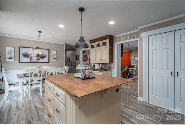 kitchen with crown molding, wooden counters, a kitchen island, a textured ceiling, and wood finished floors