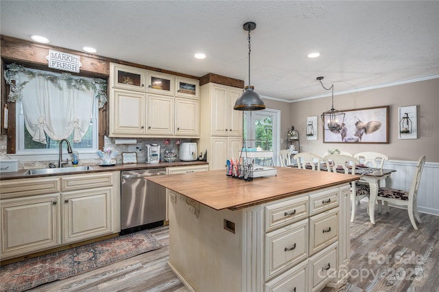 kitchen with butcher block countertops, ornamental molding, stainless steel dishwasher, light wood-style floors, and a sink