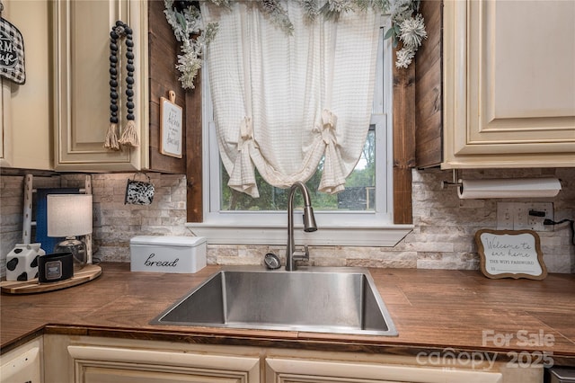 kitchen featuring dark countertops, a sink, backsplash, and cream cabinets