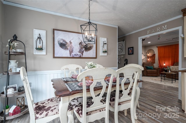 dining area with a wainscoted wall, ornamental molding, wood finished floors, a textured ceiling, and a notable chandelier