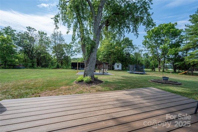 wooden deck featuring a trampoline, a lawn, and a playground