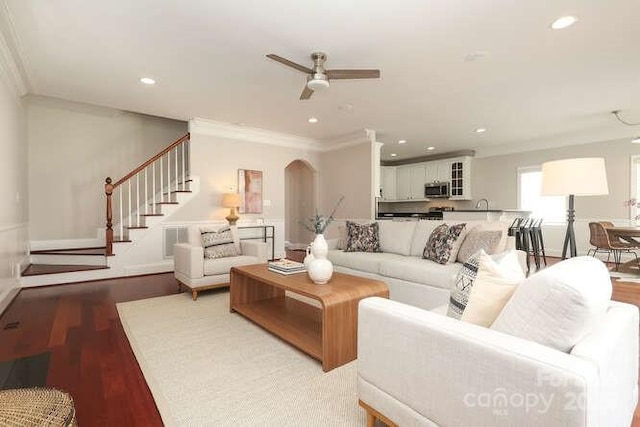 living area with arched walkways, crown molding, and wood finished floors