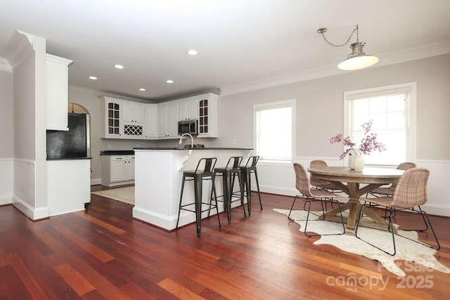 kitchen with refrigerator, ornamental molding, stainless steel microwave, dark countertops, and glass insert cabinets