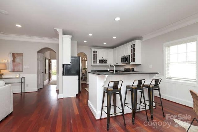 kitchen featuring arched walkways, dark wood-style floors, glass insert cabinets, ornamental molding, and a sink