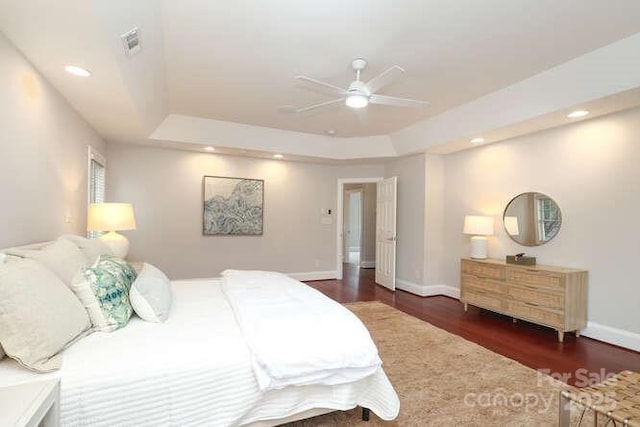 bedroom featuring a tray ceiling, visible vents, baseboards, and wood finished floors